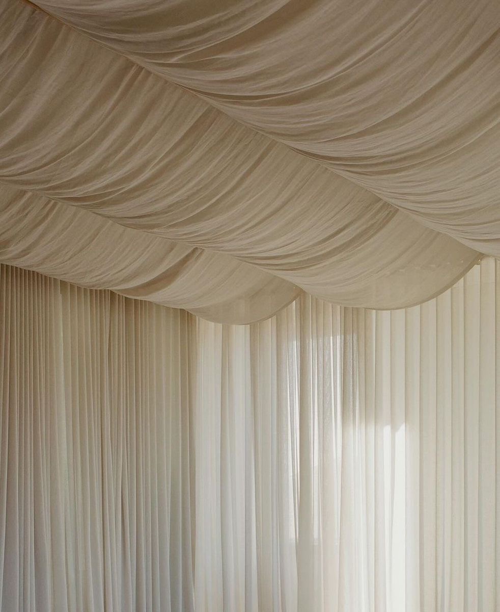 Sheer cream curtains billowing softly across a high ceiling in warm light
